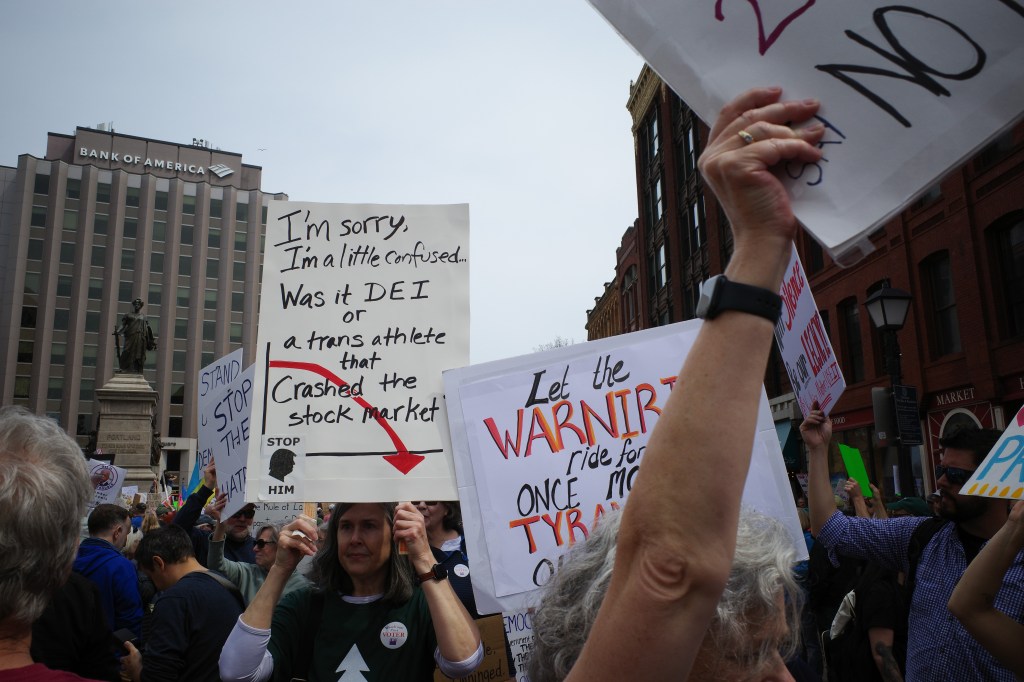 Monument Square protest in Portland, ME. Sign reads: "I'm sorry, I'm a little confused... Was it DEI or a trans athlete that crashed the stock market?"