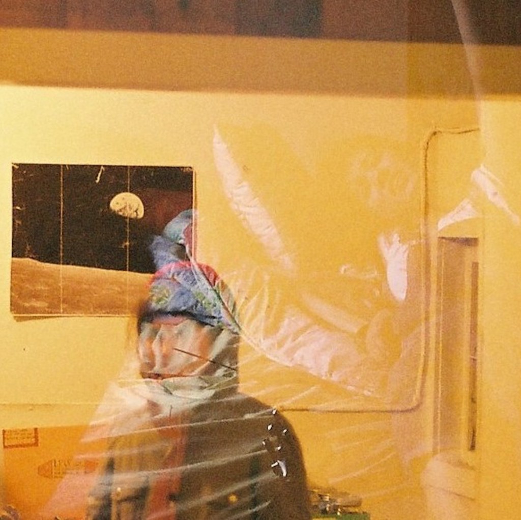 Album artwork for Planet Made of Diamonds Twice the Size of Earth! by Maine-based musician Alex Silver and Rhode Island-based musician Sarah Hopp. Hopp stands, face obscured by a winter coat and the double exposure of the film image, in front of a photo of the earth from the moon. Background is a muted yellow.